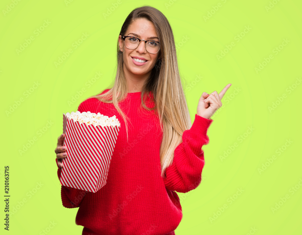 Sticker beautiful young woman eating popcorn very happy pointing with hand and finger to the side