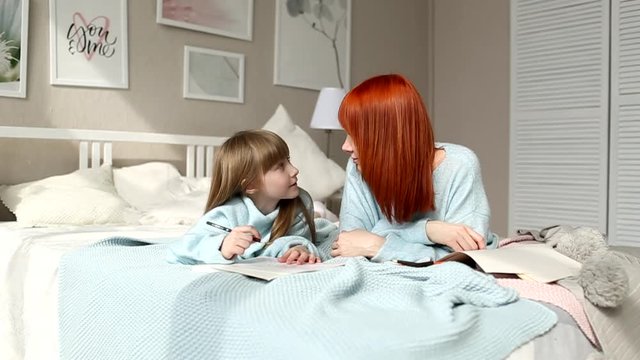Mom and daughter are lying on the bed and talking