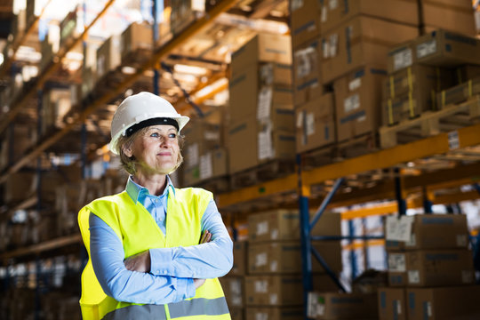 Senior woman manager or supervisor standing in a warehouse, arms crossed.