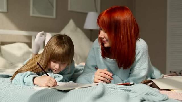 The daughter and mother lie talking and draw lying on the bed