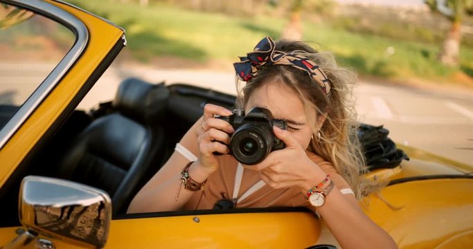 Young woman in convertible car taking photos with camera