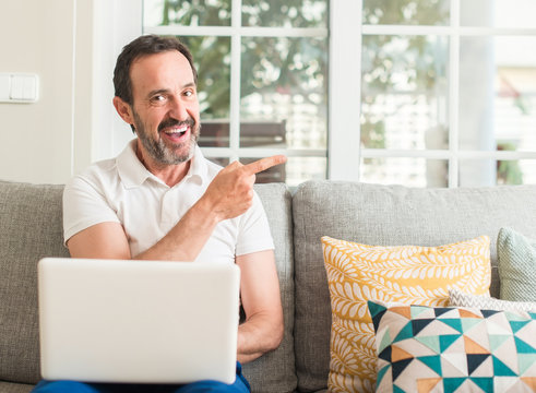 Middle age man using laptop at sofa very happy pointing with hand and finger to the side