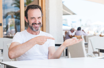Handsome senior man sitting at terrace very happy pointing with hand and finger