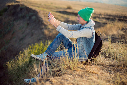 Hipster young man sits and takes a selfie on the brink of break  . Instagram stylization.