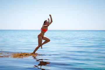 A girl is jumping into the sea water. Summer mood. Vacation at sea. Beautiful jump of a young woman in a swimsuit. Fuss and fun.