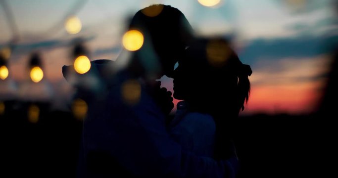 Silhouette of two lovers. Romantic date. The guy is softly kissing hands of his loving girlfriend and tenderly hugging during the sunset. 4k footage.