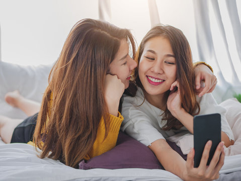 Young asian woman lesbian couple smiling happiness on the bed at home using smart phone self-portrait take a photo, Lifestyle female couple lovely.