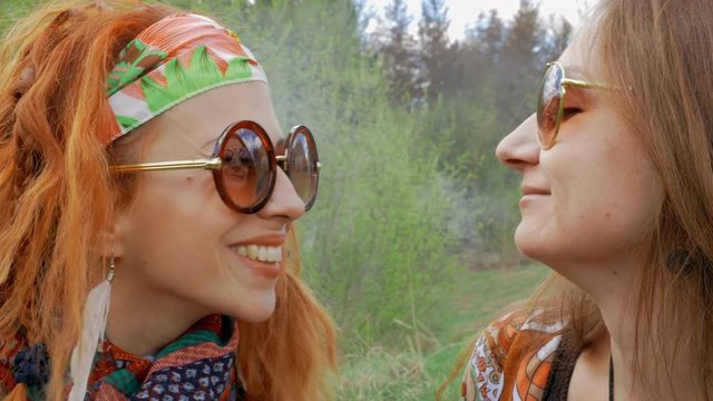Cheerful funny hippie girls blows smoke of vape and smiling in spring park close-up
