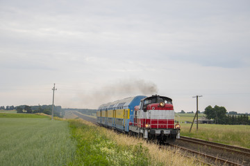 Fototapeta na wymiar Stara lokomotywa z wagonami piętrowymi pędzi przez pole