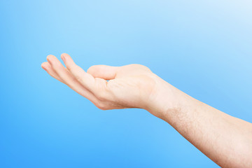 Closeup empty male hand making holding gesture with opened palm isolated at blue background.