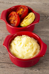 wo red pots with mashed potatoes and fried vegetables. Red pepper and parsley. Fork, knife and spoon. Wooden background. Copyspace. Vertical shot.