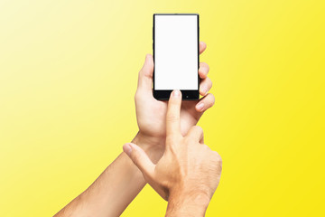 Mockup of male hand holding frameless cellphone and swiping blank white screen isolated at yellow background.