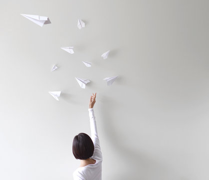 Rear view of woman throwing white paper airplanes in the air