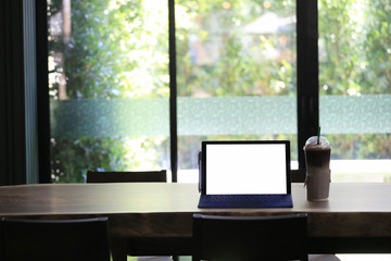 Empty screen of laptop and cold coffee mug placed on a food table in a coffee shop.