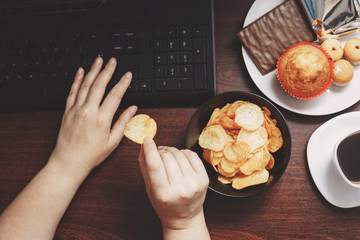 Unhealthy snack at workplace. Hands of woman working at computer and taking chips from the bowl....