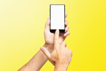 Fototapeta na wymiar Mockup of male hand holding frameless cellphone and swiping blank white screen isolated at yellow background.