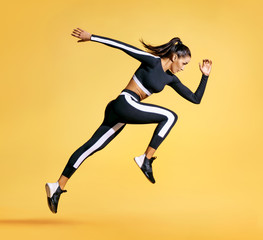 Sporty woman runner in silhouette on yellow background. Photo of attractive woman in fashionable sportswear. Dynamic movement. Side view. Sport and healthy lifestyle - obrazy, fototapety, plakaty