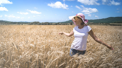 Naklejka na ściany i meble Agriculture: a girl in a straw hat inspects a wheat field with ripe ears. Sunny weather, blue sky, clouds.