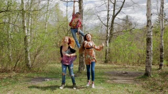 Hippie girls and boy sings and dancing in the spring forest during picnic
