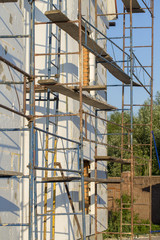 The process of building wall insulation using polystyrene in the open air. Scaffold on house, renovation. House for renovation with the scaffolding for workers on building