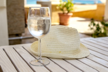 hat and glass with water and ice on a white wooden table on a sunny summer day