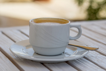 white cappuccino cup on a white wooden table on a sunny summer