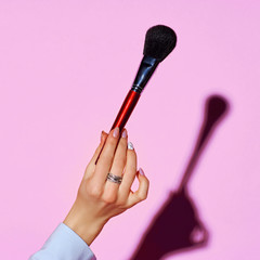 Closeup of female hand holding makeup brushes against purple background. Hard lightining with shade