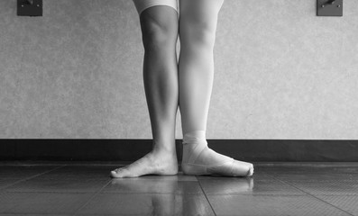Black and white version of Two sides to a ballerina, one leg wearing her ballet slipper pointe shoe on one foot, and one leg bare