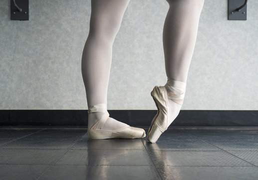 Ballet dancer warming up her feet in her pointe shoes for ballet class