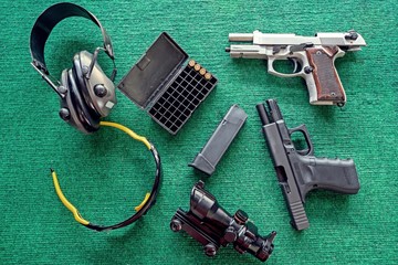 Top view weapons : Two pistols, Ear Muffs and bullets and Semi-automatic gun for self-defense on green table