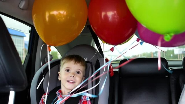 Happy child riding in a car. Festive mood, smile, laughter. Balloons in the car. Child's birthday