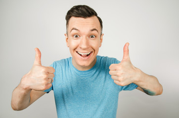 Young guy shows thumbs up dressed in a blue t-shirt on a light background.