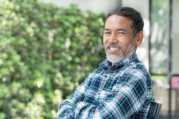 Portrait smiling attractive mature asian man retired with stylish short beard sitting outdoor at coffee shop. Close up of old happy handsome businessman or entrepreneur in urban lifestyle concept.