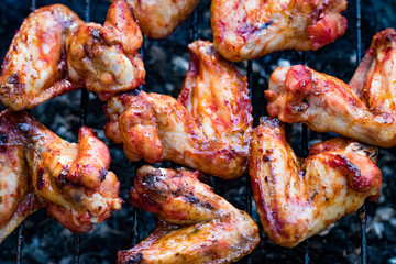 Spicy marinated chicken wings grilling on a summer barbecue with hot flames in a close up view