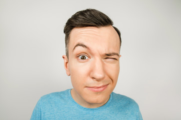 Young winking guy dressed in a blue t-shirt on a light background.