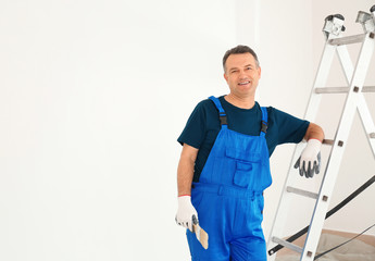Male painter in uniform with brush near ladder indoors