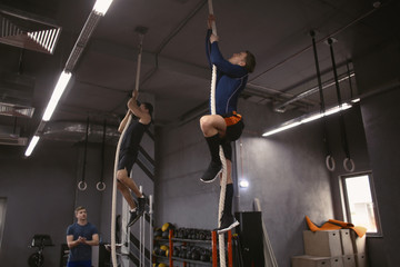 Sporty young men climbing on rope in gym