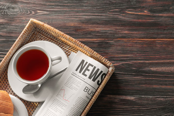 Tray with newspaper and cup of tea on wooden background
