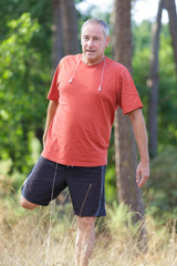 mature male athlete runner stretching in the forest