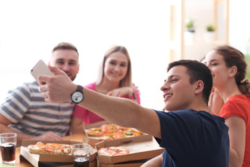Young people with pizza taking selfie indoors