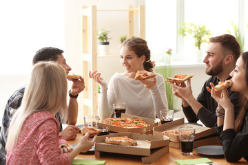 Young people eating pizza at table indoors