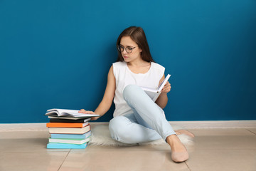 Young woman reading book on floor near color wall