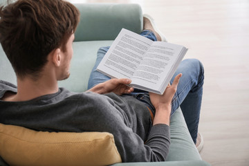 Young man reading book while resting at home