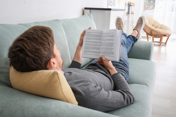 Young man reading book while resting at home