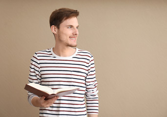 Young man with book on color background