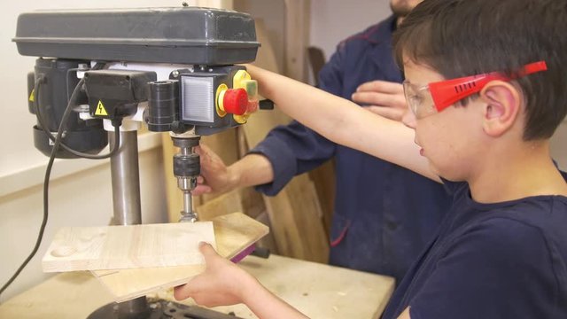 Teenager boy with his dad drills the wooden plank using industrial joinery machine in workshop