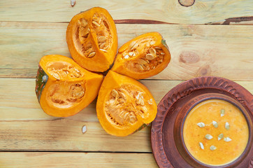 Pot pumpkin soup decorated with sliced pieces of yellow pumpkin and seeds on the wooden background. Traditional autumn food or thanksgiving dish. Top view