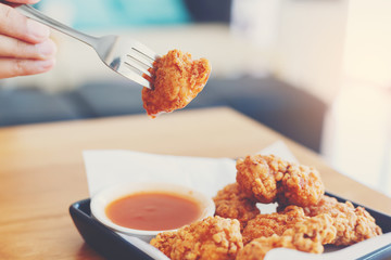 Hand of woman using a fork for take a fried chicken dipping to chilli sauce.