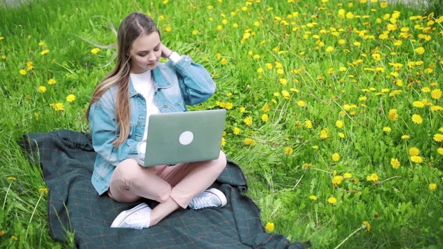 woman sitting in park on the green grass with laptop, notebook. Student studying outdoors