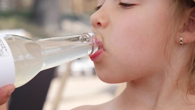 Closeup face little child girl drinks sweet sugary carbonated drink from the bottle